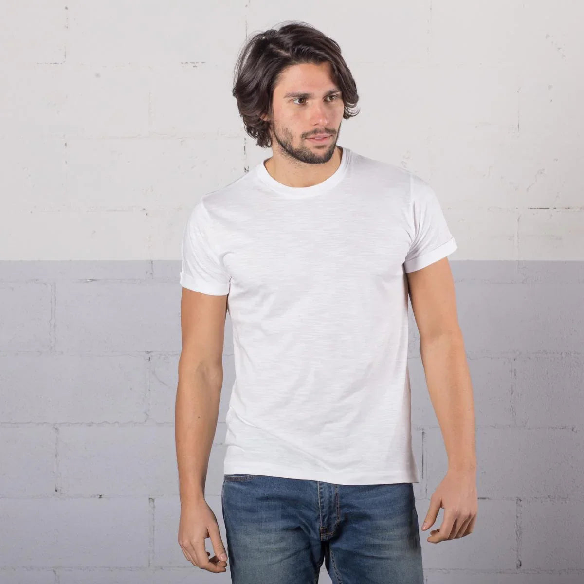 Uomo indossa t-shirt bianca in cotone effetto slub, stile streetwear, abbinata a jeans blu.