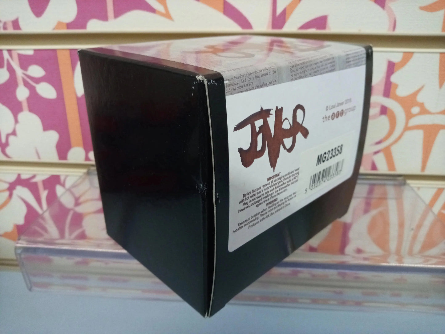 Scatola nera lucida con etichetta bianca, codice MG23358, su sfondo decorativo urban.