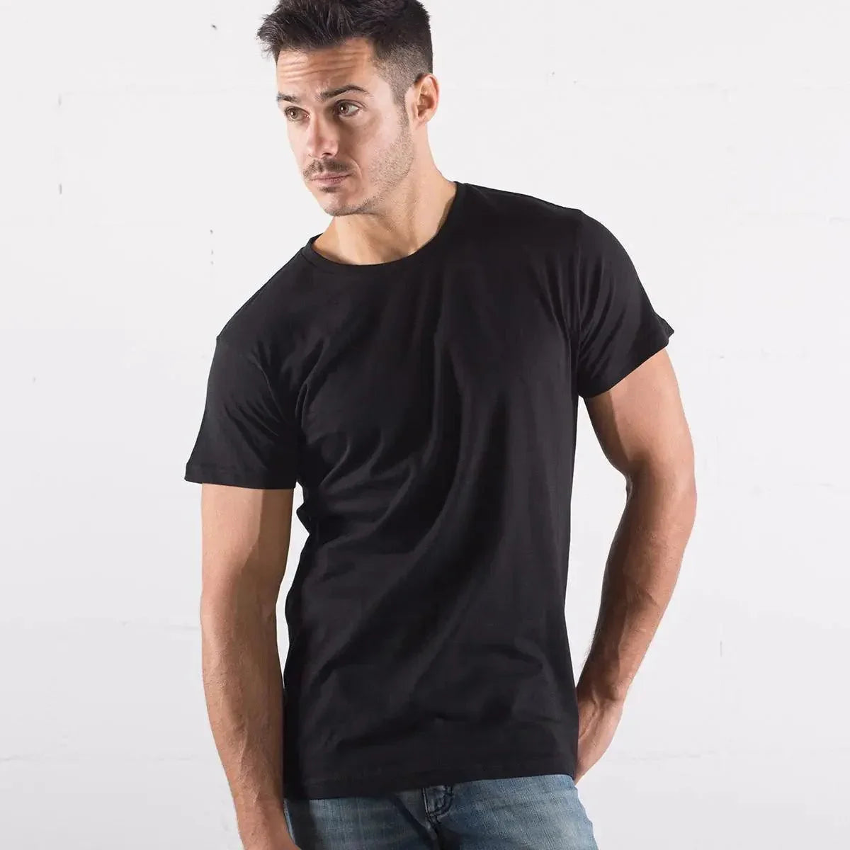 Uomo con t-shirt nera in cotone organico, stile streetwear, abbinata a jeans chiari.