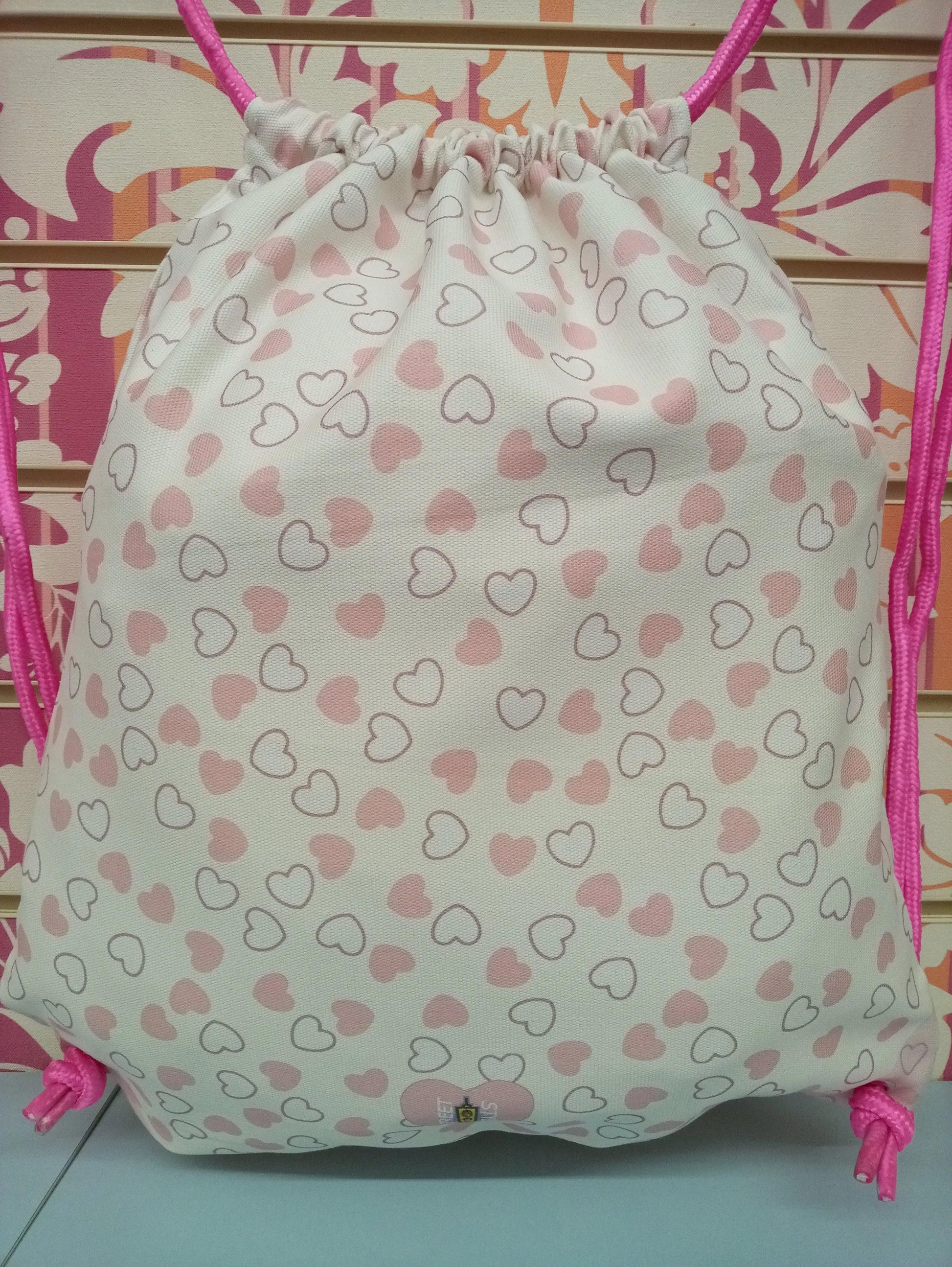 Zaino a sacca bianco con cuori rosa, cordini fucsia, stile streetwear urban, tessuto canvas.
