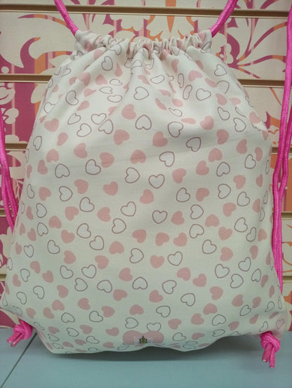 Zaino a sacca bianco con cuori rosa, cordini fucsia, stile streetwear urban, tessuto canvas.