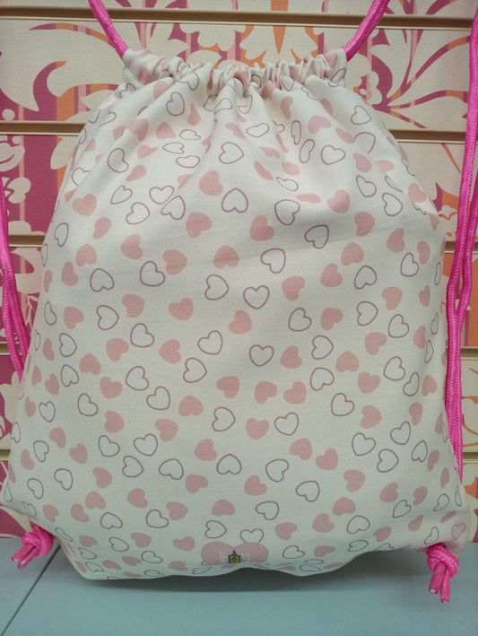 Zaino a sacca bianco con cuori rosa, cordini fucsia, stile streetwear urban, tessuto canvas.