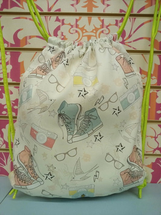 Zaino a sacca urban in tessuto bianco con stampe colorate streetwear di scarpe, fotocamere e occhiali, lacci fluo verdi.