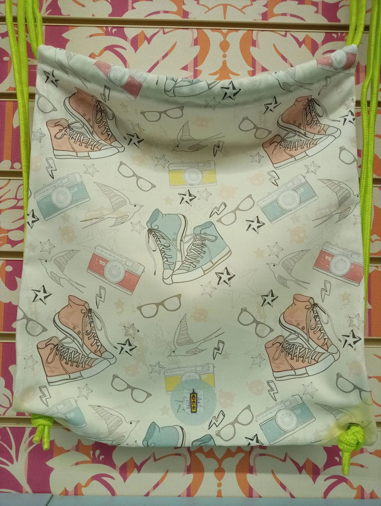 Zaino a sacca streetwear in tessuto con stampa urban, sneakers, occhiali e fotocamere colorate, cordini verde fluo.