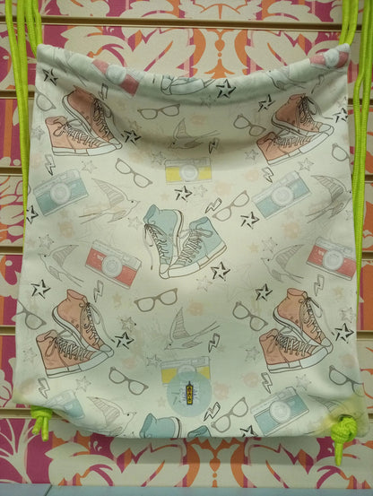 Zaino a sacca streetwear in tessuto con stampa urban, sneakers, occhiali e fotocamere colorate, cordini verde fluo.