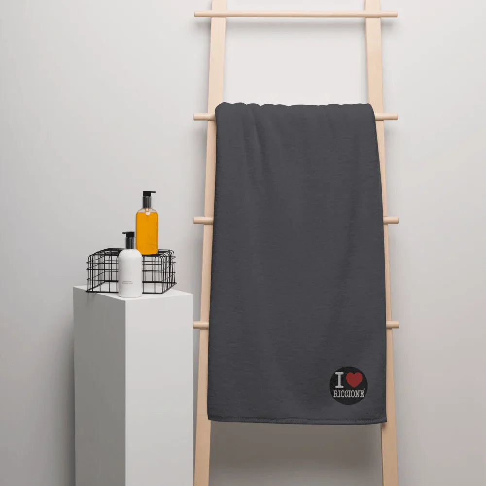 Asciugamano oversize in cotone turco grigio scuro con scritta I Love Riccione, stile streetwear urban, appeso a una scala in legno.
