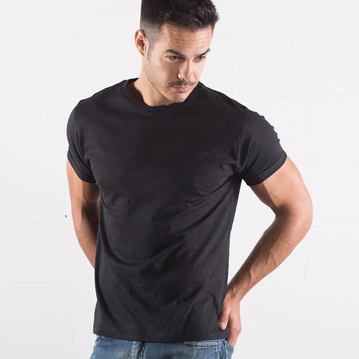 Uomo indossa t-shirt nera in cotone, stile streetwear, abbinata a jeans blu, look urban casual.